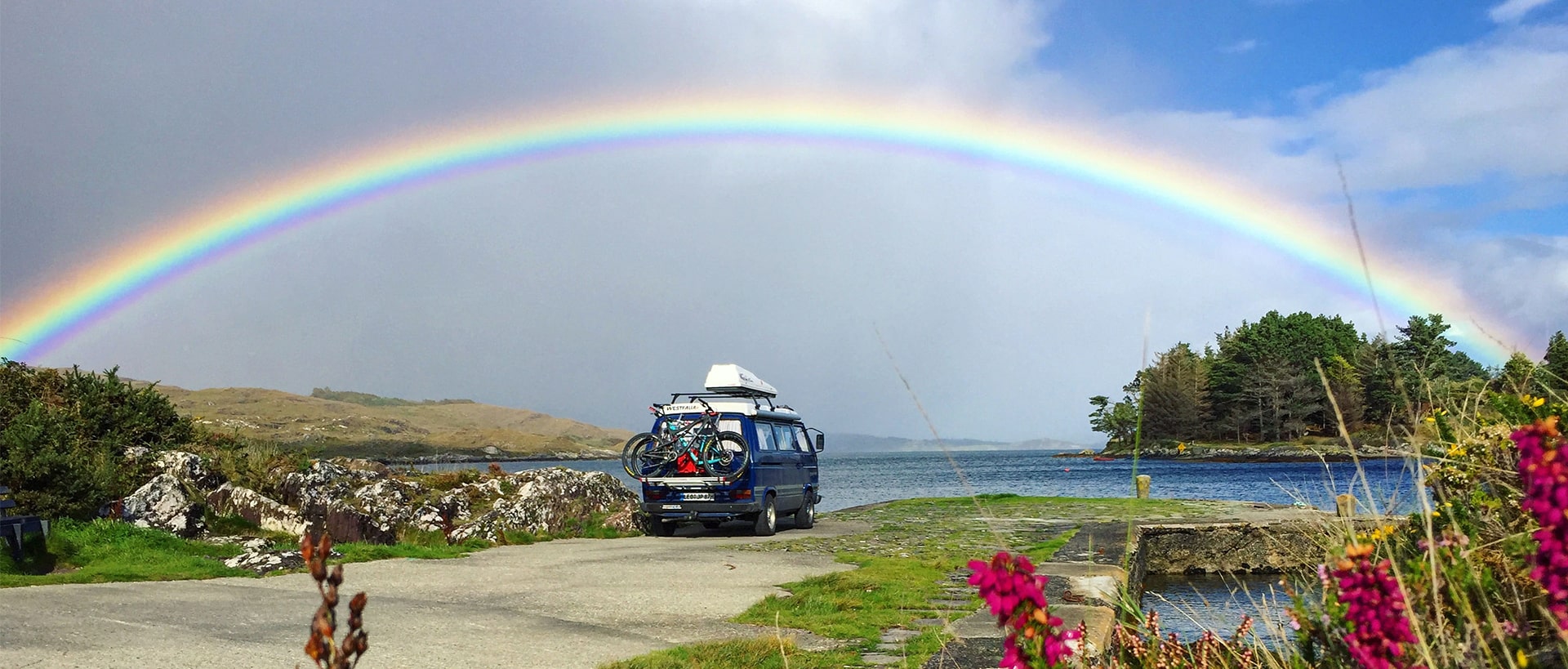 Campervan steht in Irland mit Regenbogen am Himmel